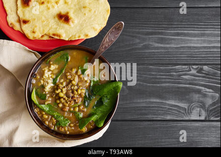 Mung dhal mit grünen Spinat am schwarzen Holz der Tischplatte. Moong Dal - Indische Küche Curry. Vegetarisches Gericht mit chapati. Kopieren Sie Raum, Ansicht von oben Stockfoto