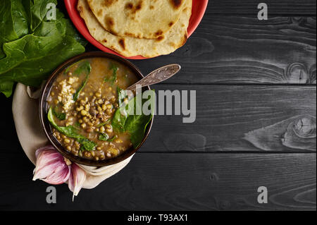 Mung dhal mit Spinat, Chapati und Knoblauch am schwarzen Holz der Tischplatte. Moong Dal - Indische Küche Curry. Vegetarische würzigen Gericht. Nach oben Ansichtskopie Raum Stockfoto