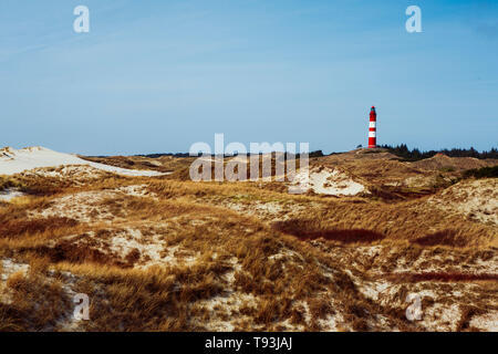 Malerische Landschaft mit roten Leuchtturm auf dem Hügel in der Ferne gegen bewölkten Himmel und trockenes Gras im Vordergrund. Idyllischer Blick aus niedrigen Winkel Stockfoto