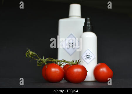 Esticides in der landwirtschaftlichen Nahrungsmittel mit roten Tomaten in den Vordergrund und blurry weißen Flaschen mit giftigen Warnhinweis auf schwarzem Hintergrund Stockfoto