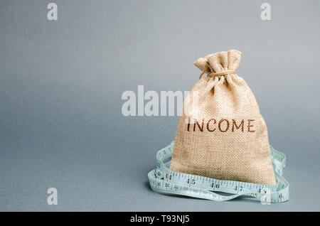 Geld beutel mit dem Wort Einkommen und Maßband. Reduzierte Einnahmen und Gewinne. Reduzierte Budgets. Verlust von Geld. Gescheiterter und Armut. Lowe Stockfoto