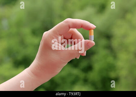 Pille in weiblicher Hand auf verschwommenes grün Natur Hintergrund, Mädchen, dass Medikamente in der Kapsel hautnah. Konzept der Apotheke, Behandlung, Vitamine Stockfoto