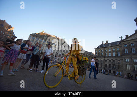 Street Performer in Gelb lackiert stehen immer noch auf einem Fahrrad sitzend in der Mitte des Dam Platzes im Stadtzentrum von Amsterdam. Stockfoto