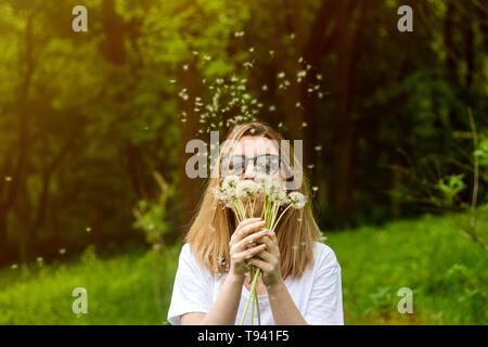 Junge Frau bläst Löwenzahn im Sommer Park. Grünen Wald schönen Hintergrund. Weiche sun Flair. Stockfoto