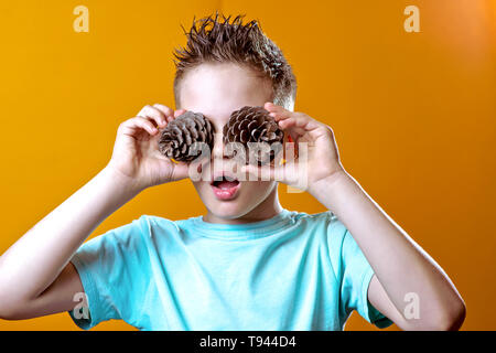 Ein Junge in einem hellen T-Shirt setzen zwei Kegel seine Augen auf einem hellen farbigen Hintergrund Stockfoto