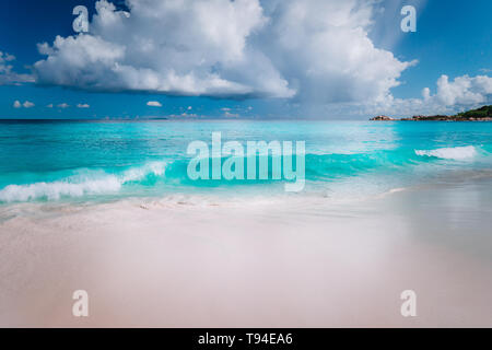 Schöne weiße Welle rollt in Richtung tropischen Sandstrand. Herrlich flauschige Wolken über dem blauen Meer. Seychellen Grand Anse, La Digue, Seychellen. Stockfoto