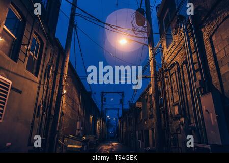 Eine schwach beleuchtete gruselige Gasse mit hellem Lichtreflexe und Blau Himmel Stockfoto