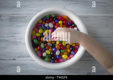 Die Hand eines Kindes nimmt Süßigkeiten von einem weißen Teller Stockfoto