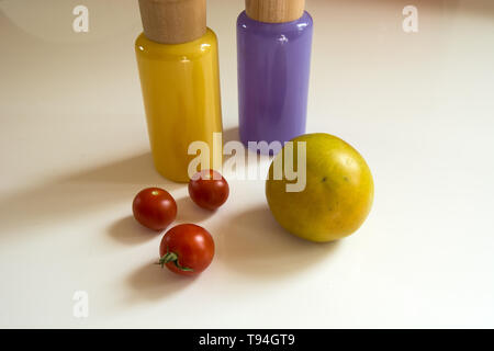 Tomaten liegen auf einem weißen Hintergrund und bunte Glasflaschen mit Elementen aus Holz Stockfoto