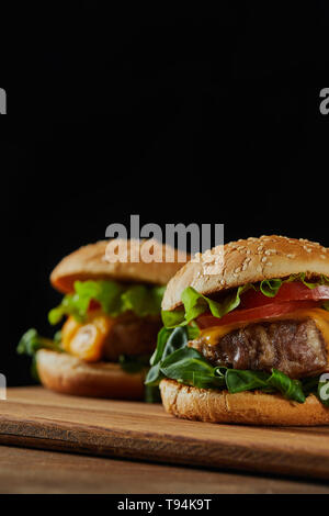 Selektiver Fokus der köstliche Fleisch Burger mit Käse und Gemüse auf Schwarz isoliert Stockfoto