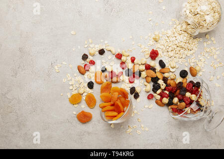 Blick von oben auf die Haferflocken, getrocknete Aprikosen und Beeren, Nüsse unordentlich auf strukturierte graue Oberfläche verstreut Stockfoto