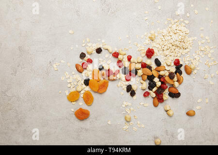 Blick von oben auf die Haferflocken, getrocknete Aprikosen und Beeren, Nüsse unordentlich auf strukturierte graue Oberfläche Tisch verstreut Stockfoto