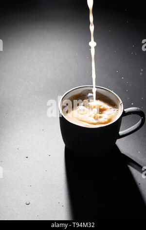 Tasse Kaffee mit Milch giessen auf dunklen texturierte Oberfläche Stockfoto