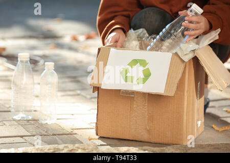 Junge Frau werfen Kunststoff Flasche in Karton im Freien. Recycling Konzept Stockfoto