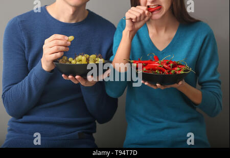 Junges Paar essen Weintrauben und Chili auf grauem Hintergrund Stockfoto