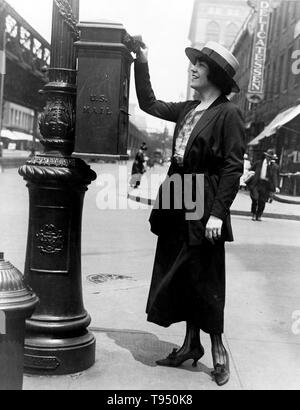 Titel: 'Merle Alcock (Metropolitan Opera Altistin) Mailing einen Brief in New York City" zeigt eine Frau mit einem Brief an ein US-Mailbox auf einen Post auf einer Straße Ecke befestigt. Ein Briefkasten, auch als Sammelbox, Mailbox, Letter Box oder Drop Box bekannt ist ein physisches Gerät, in der die Mitglieder des öffentlichen ausgehende E-Mail wird für die Sammlung durch die Agenten der Postdienste in einem Land Service vorgesehen. Stockfoto