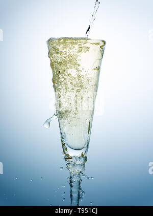 Gießen und Überfüllung von Champagner auf ein schickes Glas vor einem blauen Hintergrund Stockfoto