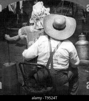 Mit dem Titel: "Butter überhaupt kommen?" zeigt eine Frau mit butterfass auf dem Schoß Mann sitzend; von hinten gesehen. 7/8 stereograph fotografiert von E.W. Kelley, 1906. Stockfoto