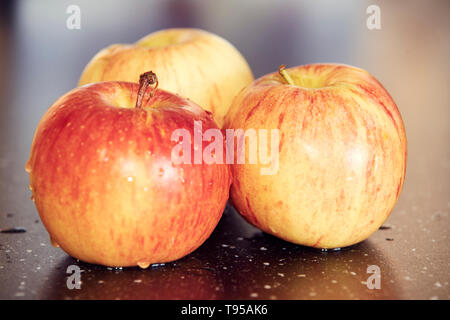 Detaillierte Makrofotografie von drei gelb-roten Äpfel auf dunklen glatten Tisch. Süße und frische Äpfel mit Wassertropfen auf dunklen Tisch mit super Bokeh. Stockfoto