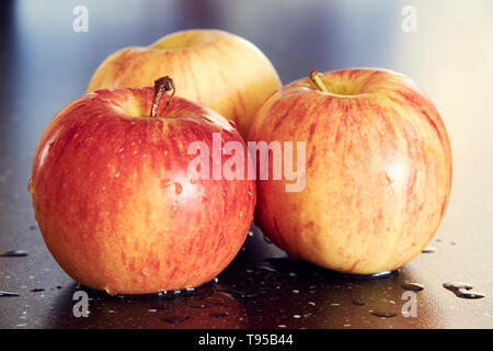 Detaillierte Makrofotografie von drei gelb-roten Äpfel auf dunklen glatten Tisch. Süße und frische Äpfel mit Wassertropfen auf dunklen Tisch mit super Bokeh. Stockfoto