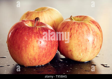 Detaillierte Makrofotografie von drei gelb-roten Äpfel auf dunklen glatten Tisch. Süße und frische Äpfel mit Wassertropfen auf dunklen Tisch mit super Bokeh. Stockfoto