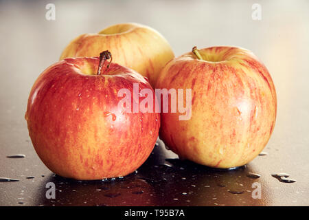 Detaillierte Makrofotografie von drei gelb-roten Äpfel auf dunklen glatten Tisch. Süße und frische Äpfel mit Wassertropfen auf dunklen Tisch mit super Bokeh. Stockfoto