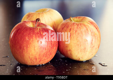 Detaillierte Makrofotografie von drei gelb-roten Äpfel auf dunklen glatten Tisch. Süße und frische Äpfel mit Wassertropfen auf dunklen Tisch mit super Bokeh. Stockfoto