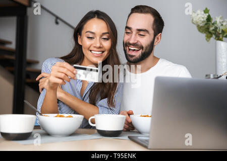 Happy multiethnischen Paar Frühstück in der Küche, am Laptop suchen, mit Kreditkarte Stockfoto
