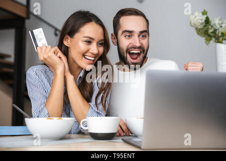 Happy multiethnischen Paar Frühstück in der Küche, am Laptop suchen, mit Kreditkarte Stockfoto