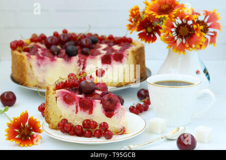 Kuchen mit Beeren ist auf einem Schild auf einem weißen Hintergrund, Stück Kuchen und eine Tasse Kaffee im Vordergrund befindet Stockfoto