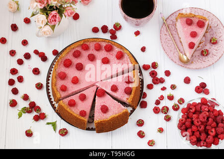 Käsekuchen mit Himbeeren ist auf einem weißen Hintergrund, Ansicht von oben, Stück Käsekuchen auf einer separaten Platte, ganz in der Nähe gibt es eine Tasse Kaffee und Stockfoto