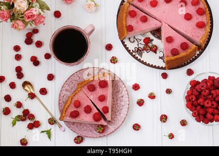 Käsekuchen mit Himbeeren ist auf einem weißen Hintergrund, Ansicht von oben, Stück Käsekuchen auf einer separaten Platte, ganz in der Nähe gibt es eine Tasse Kaffee und Stockfoto