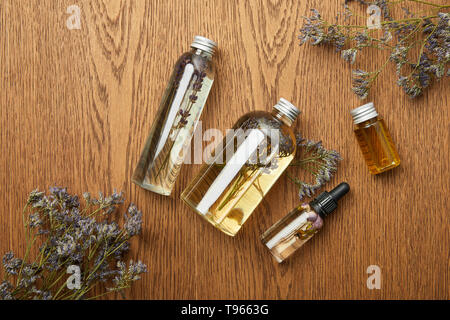 Blick von oben auf die durchsichtigen Flaschen mit organischen Schönheit Produkte in der Nähe von getrockneten Kräutern auf hölzernen Hintergrund Stockfoto