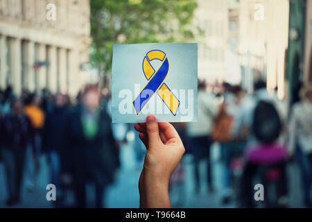 Welt Down-syndrom Tag als Hand hält ein Blatt Papier mit Blau Gelb awareness Ribbon Symbol überfüllten Straße Hintergrund. Keine Diskriminierung conce Stockfoto