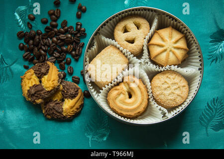 Cookies mit Zucker in einem runden Feld und zwei Liegen auf einem grün Tischdecke mit Kaffeebohnen Stockfoto