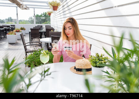 Frau Sommer Cafe, Hand Phone, zahlt mit Kreditkarte kaufen, bestellt Ware, schreibt aus Geld vom Konto. Das kontaktlose Bezahlen, Frühstück, Mittagessen. Die Stockfoto