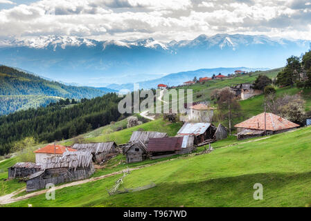 Bewölkt Frühling über höchste Dorf am Balkan und in Bulgarien - Ortsevo in Rhodopen Gebirge. Hohe verschneite Pirin Gebirge im Hintergrund. Stockfoto