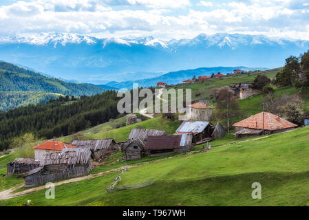 Bewölkt Frühling über höchste Dorf am Balkan und in Bulgarien - Ortsevo in Rhodopen Gebirge. Hohe verschneite Pirin Gebirge im Hintergrund. Stockfoto