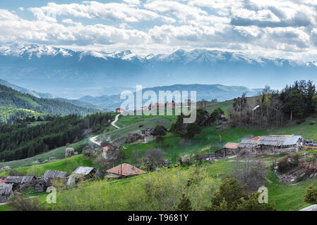 Bewölkt Frühling über höchste Dorf am Balkan und in Bulgarien - Ortsevo in Rhodopen Gebirge. Hohe verschneite Pirin Gebirge im Hintergrund. Stockfoto