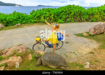 Happy kaukasischen Lifestyle touristische Frau auf dem Fahrrad in der Nähe von Anse Banane in La Digue, Seychellen, mit Riesenschildkröte, Aldabrachelys gigantea Stockfoto