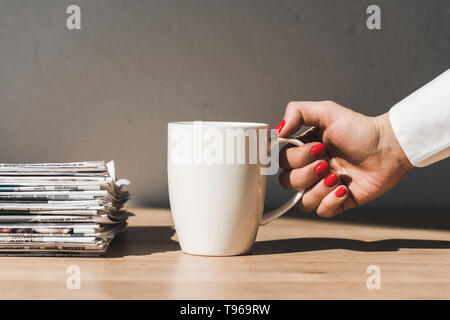 7/8-Ansicht von Frau mit weißer Schale auf Holztisch in der Nähe von Pile verschiedener Zeitungen Stockfoto