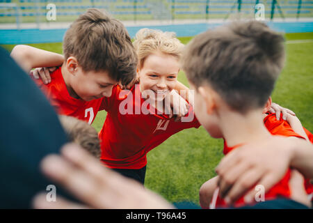 Glückliche Kinder, Sport. Gruppe von Happy Boys machen Sport drängeln. Lächelnde Kinder gemeinsam mit Trainer auf Gras Sportplatz. Jungs reden w Stockfoto