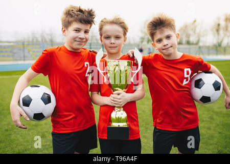 Jugendliche gerne Fußball-Spieler nach dem Spiel. Jungen und goldene Schale und Fußbälle. Sport Portrait von drei glückliche Fußball Spieler. Sie Fußball Stockfoto