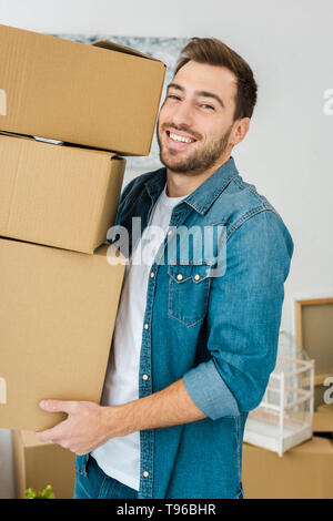 Freudiger Mann in Jeans Jacke, Kartons und Kamera Stockfoto