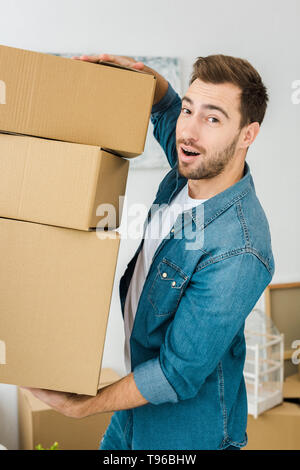 Freudiger Mann in Jeans Jacke, Kartons und Kamera Stockfoto