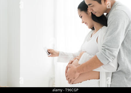 Schöne Asiatische schwangere Frau und Asiatischen gutaussehenden Mann Holding und suchen ein sonogramm im Haus. Konzept der Schwangerschaft, Gesundheit, Gynäkologie, medi Stockfoto