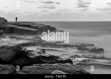 Einsamer Mann auf Misty rock Ocean Shore Stockfoto