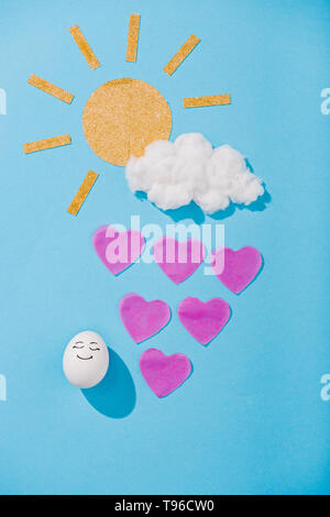 Blick von oben auf die Papier sun, Zuckerwatte Cloud, Ei mit glücklichen Gesichtsausdruck und Herzförmigen Regentropfen auf Blau Stockfoto