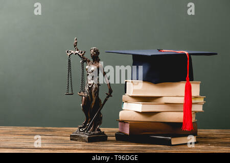 Stapel von Büchern, Themis statuette und akademischen Kappe auf Holz- Oberfläche auf Grau Stockfoto
