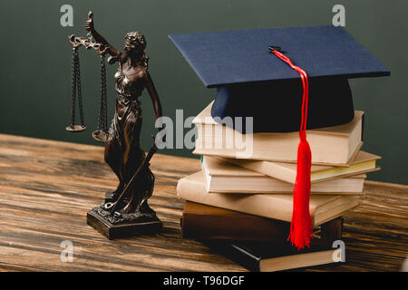Themis Statuette, Stapel von Büchern und akademischen Kappe auf Holz- Oberfläche auf Grau Stockfoto